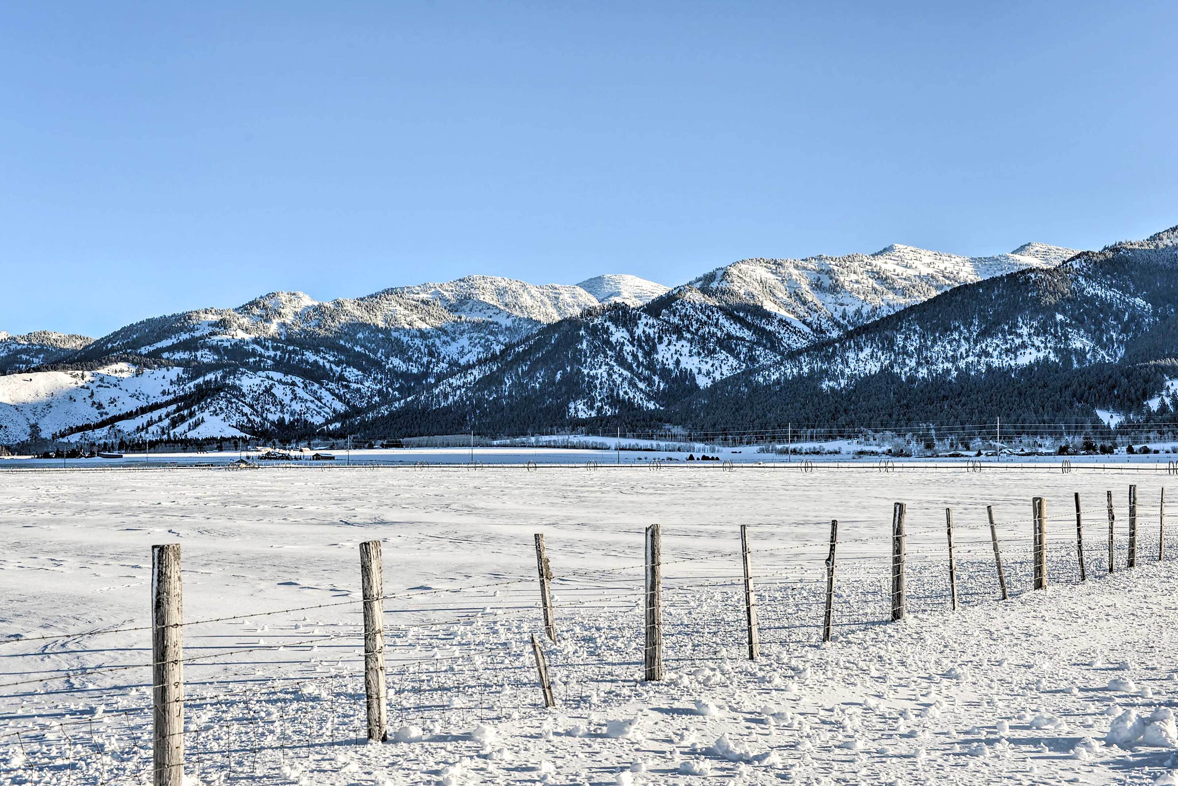 Campo nevado con una valla de madera y montañas al fondo.