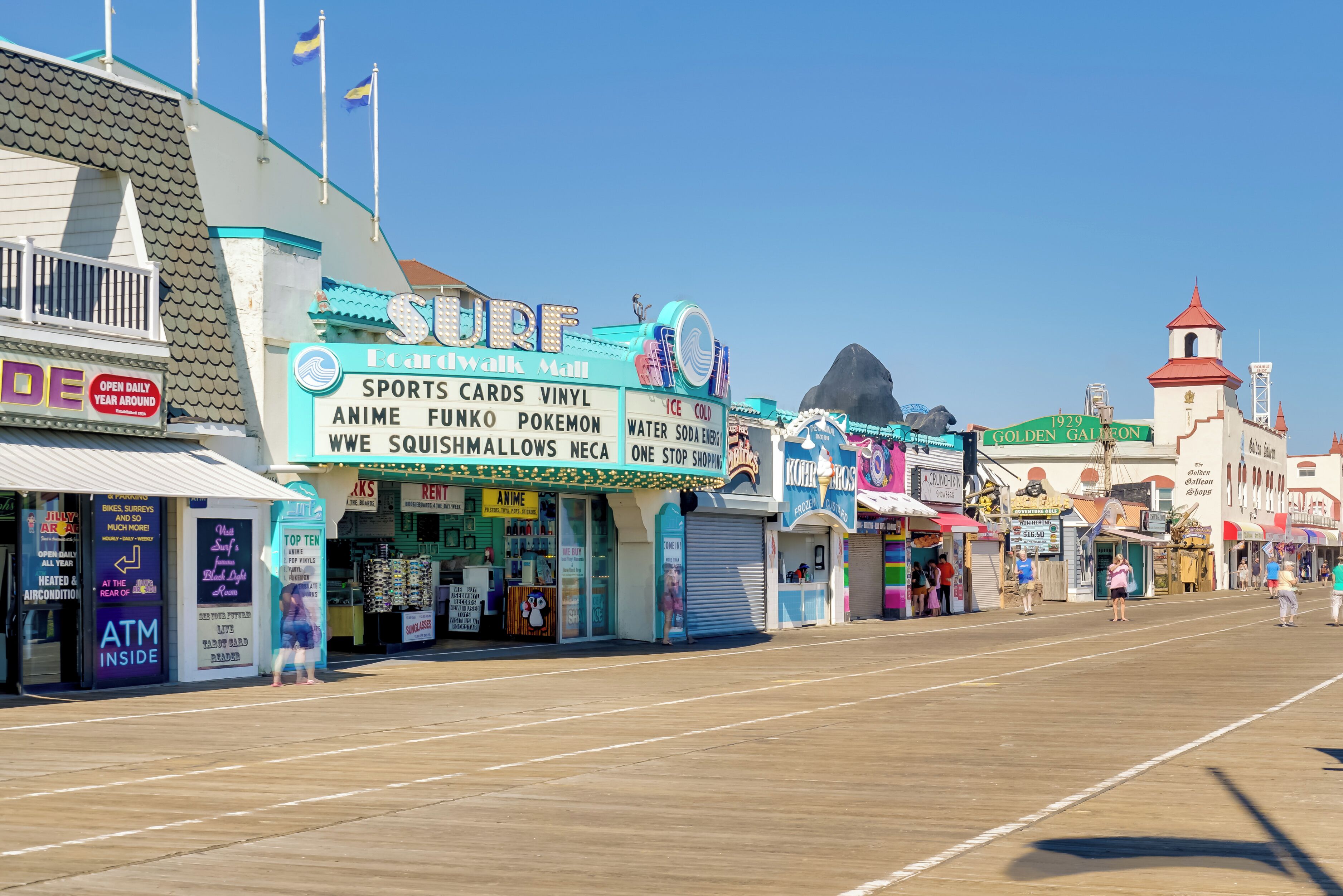 A boardwalk with various shops, including a surf shop, and a historic building with a red roof.