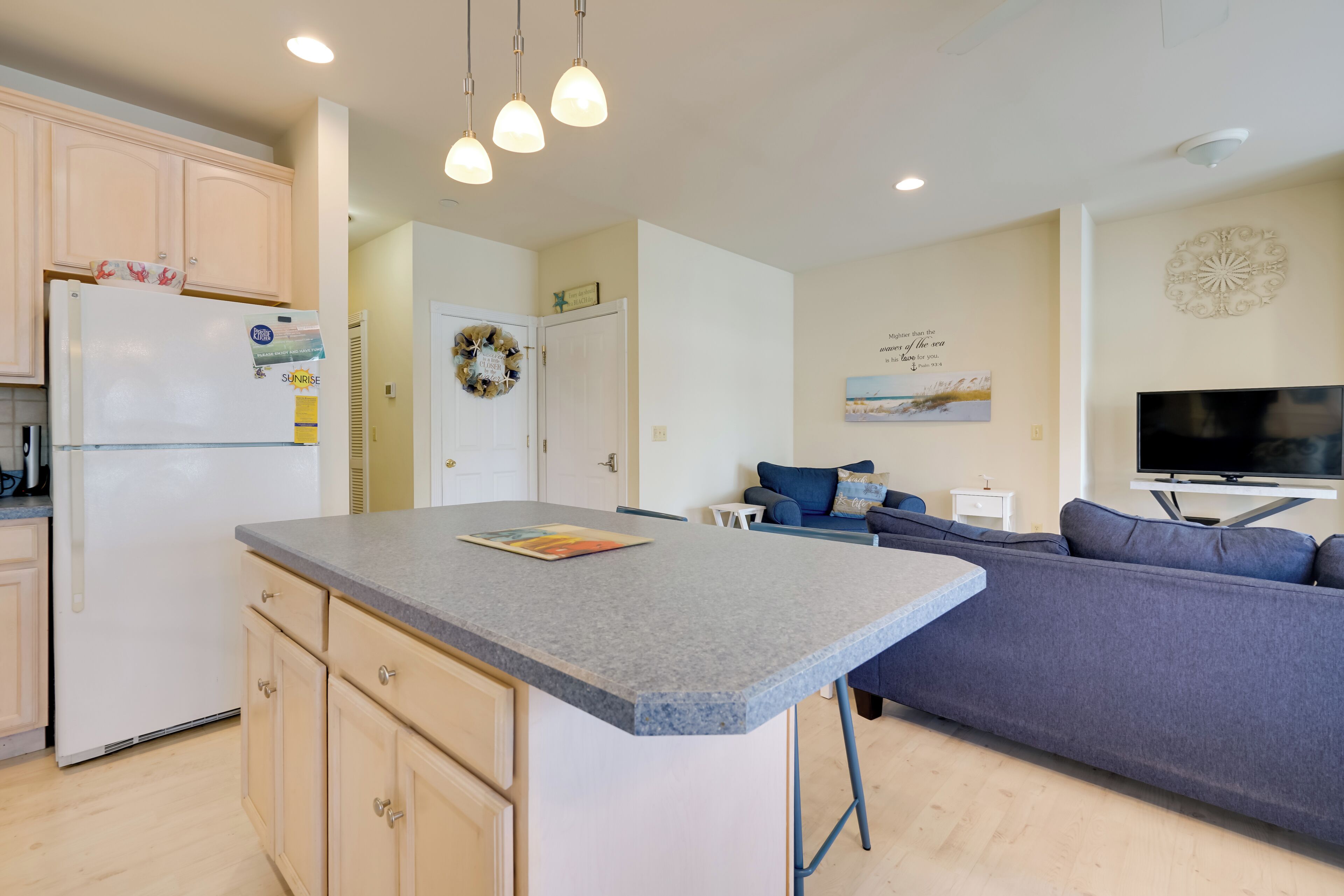 A modern kitchen with a central island, a built-in refrigerator, and a dining area with a blue sofa and a flat-screen TV.