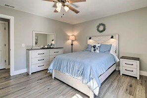 Quarto com cama, mesas de cabeceira, cômoda, espelho, ventilador de teto e um guirlanda pendurada na parede.
