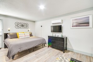 Een slaapkamer met een bed, een dressoir, een airconditioner, kunstwerken en een decoratief wandobject.