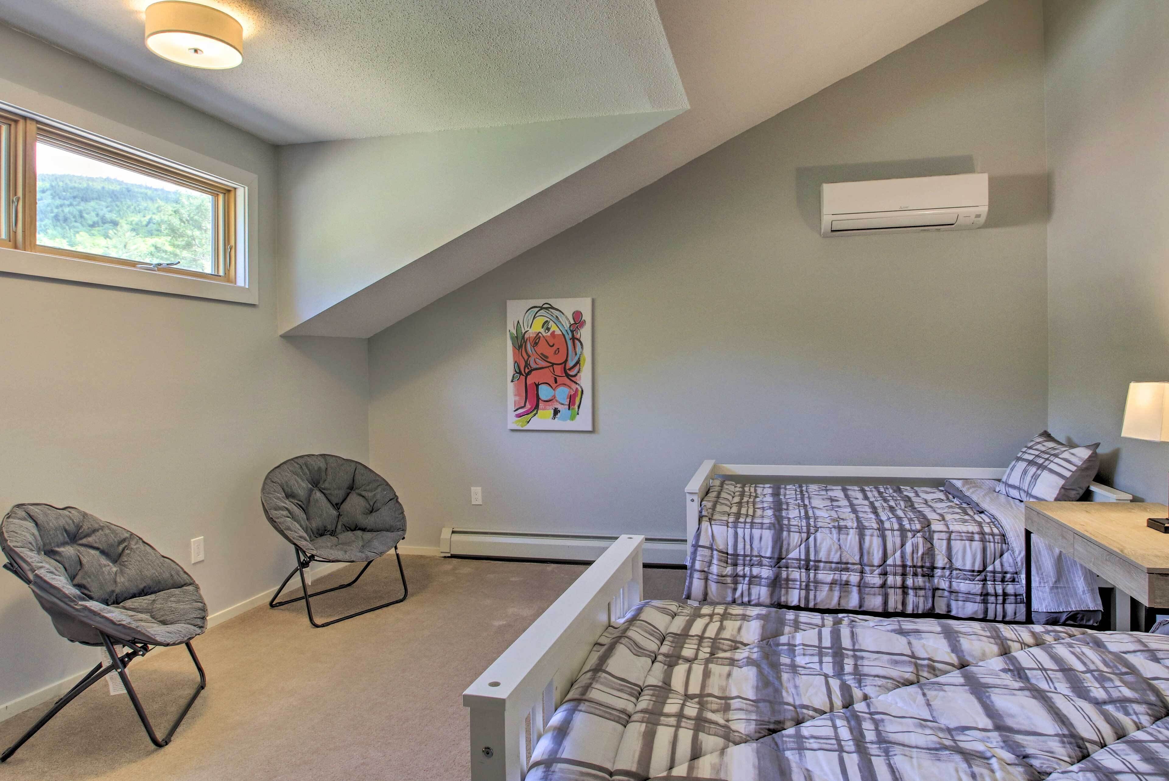 A bedroom with two beds, a window, an air conditioner, and a colorful painting on the wall.