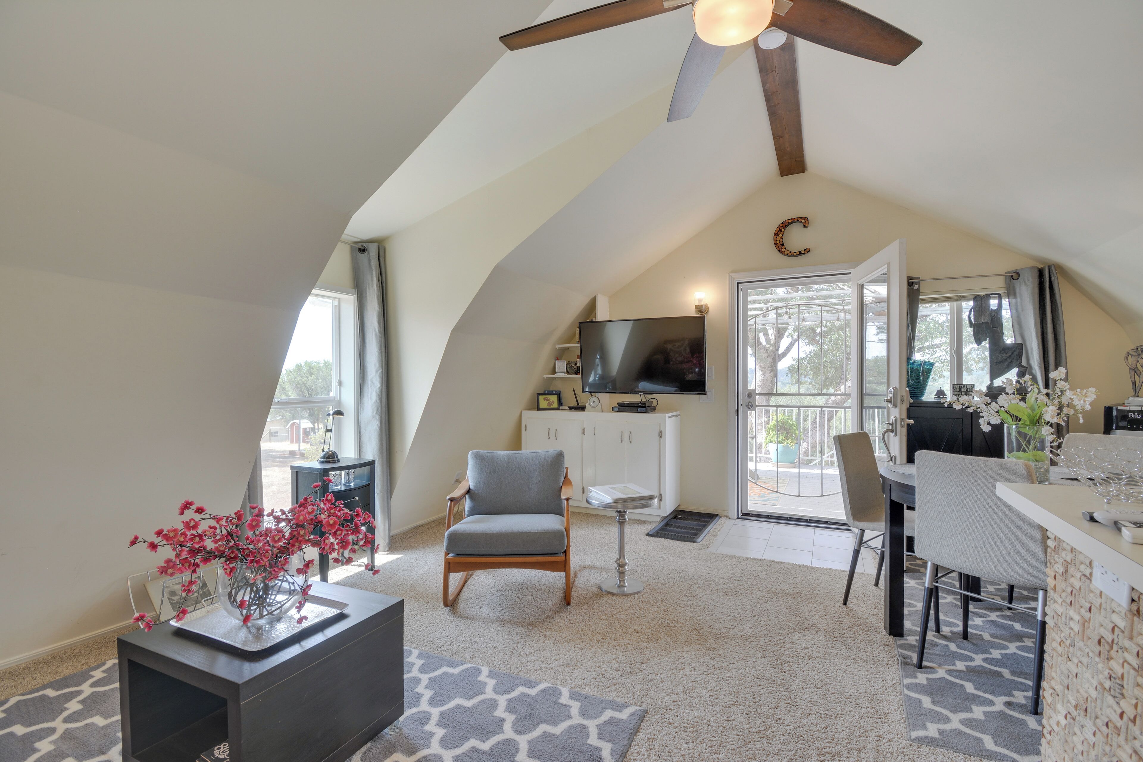 A spacious loft with a high ceiling, a ceiling fan, a large window, a dining area, and a kitchen.