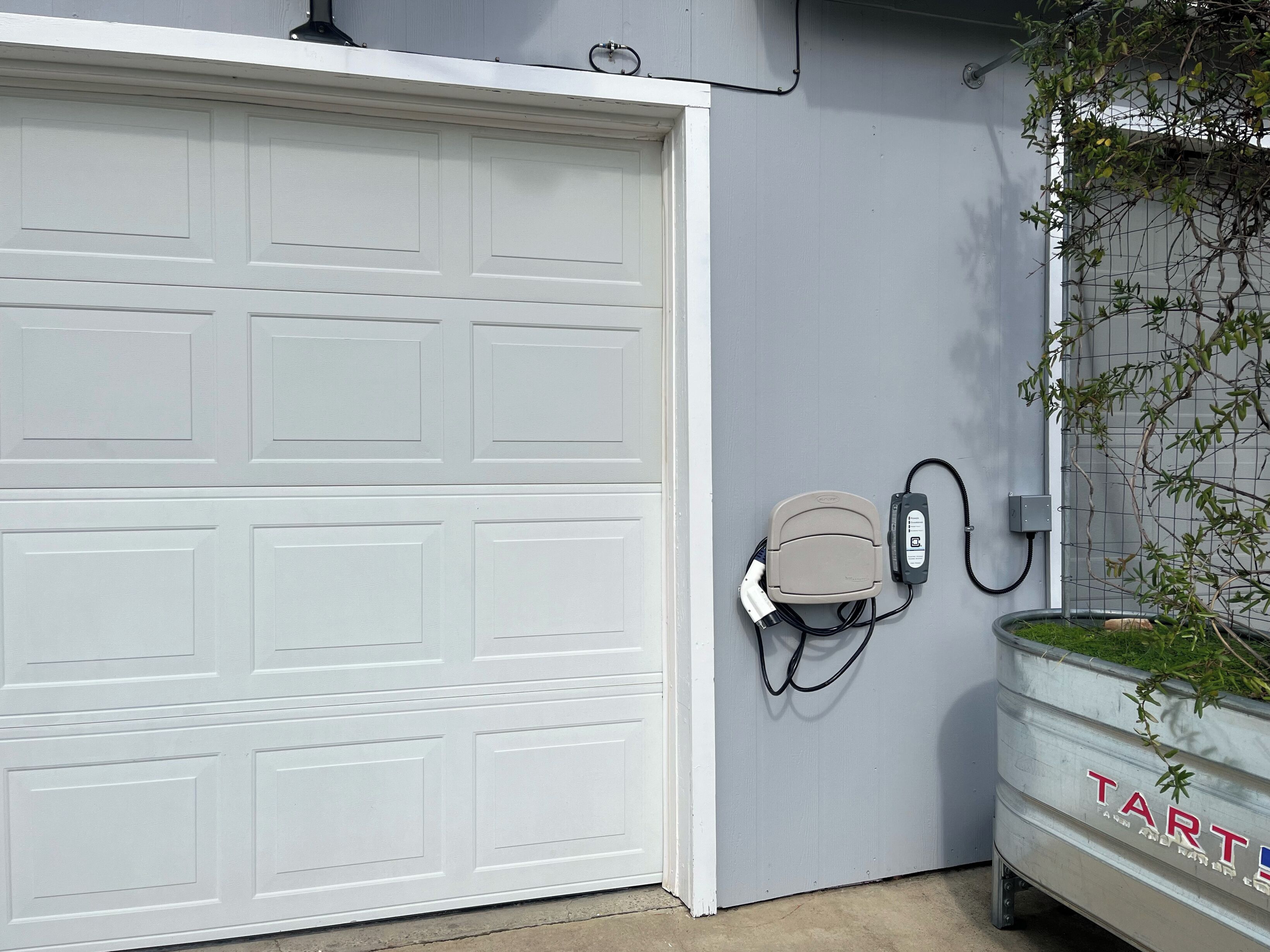 Un garage con una porta bianca, una presa di corrente a muro e un vaso con piante verdi.