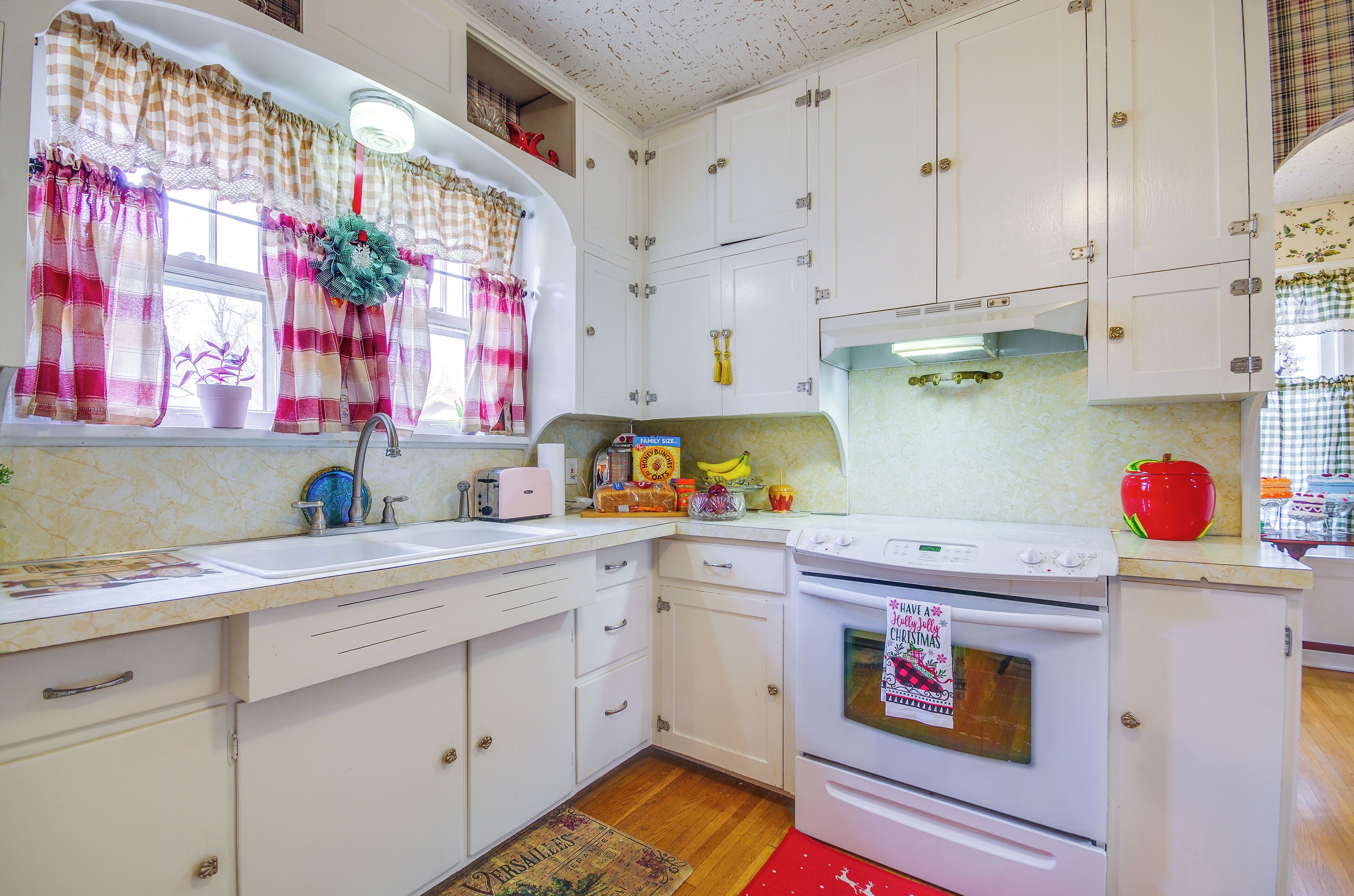 A kitchen with white cabinets, a stove, and a window with curtains.
