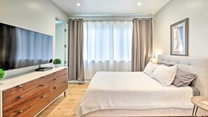 Een moderne slaapkamer met een groot bed, een flatscreen televisie, een houten dressoir en een raam met gordijnen.