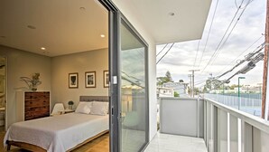 Een slaapkamer met een bed, een nachtkastje, een dressoir en een glazen schuifdeur die leidt naar een balkon met uitzicht op de stad.