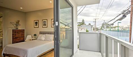 Un dormitorio con cama, mesita de noche, cómoda y puerta corrediza de vidrio que da a un balcón con vistas a la ciudad.