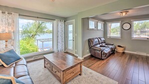 A spacious living room with a leather sofa, a wooden coffee table, and a view of a lake through large windows.