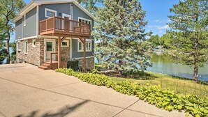 A two-story house with a balcony, a stone foundation, and a view of a lake.