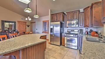 A kitchen with granite countertops, wooden cabinets, stainless steel appliances, and pendant lighting.