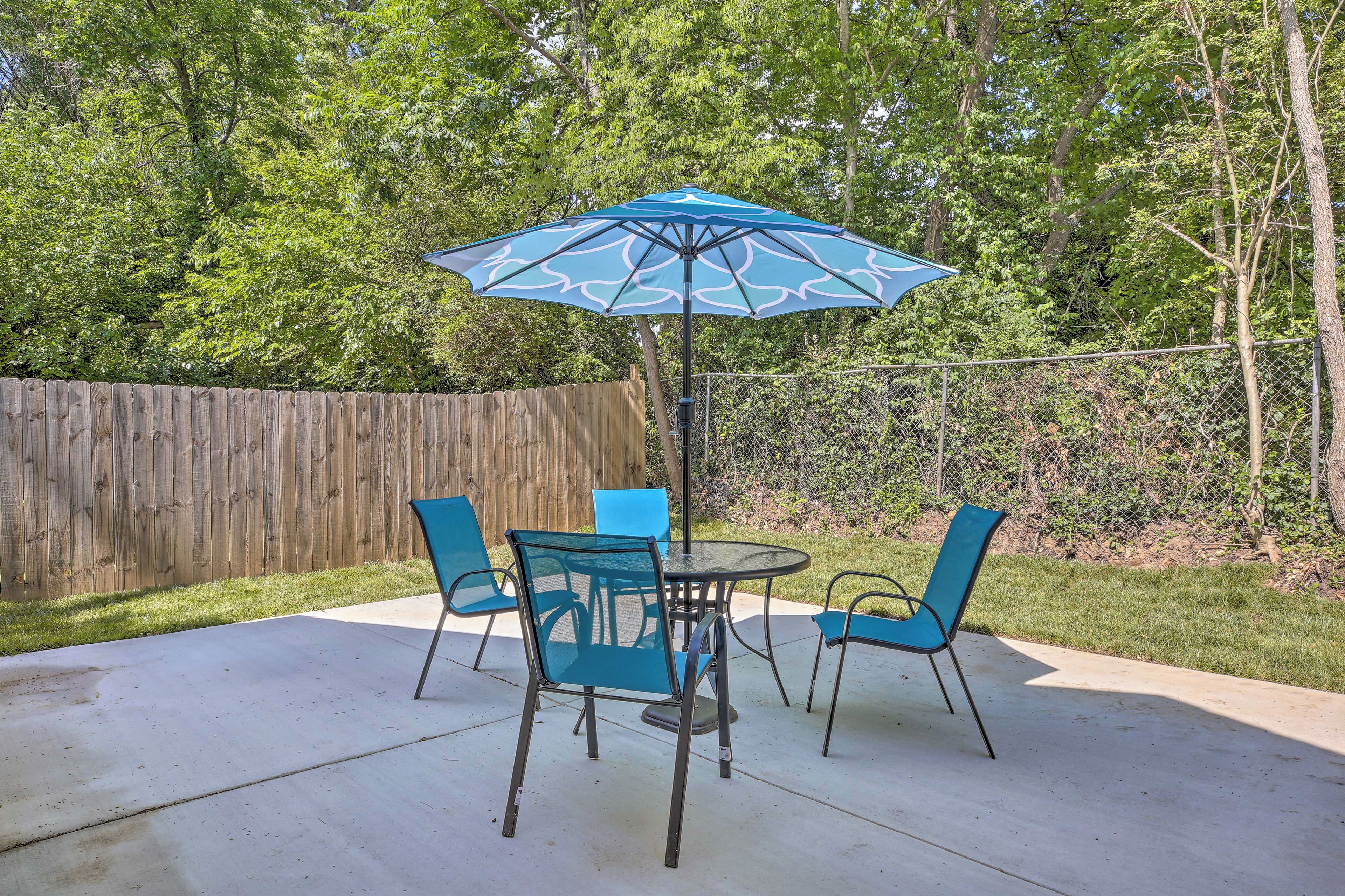 A patio with a table and chairs, an umbrella, and a wooden fence.