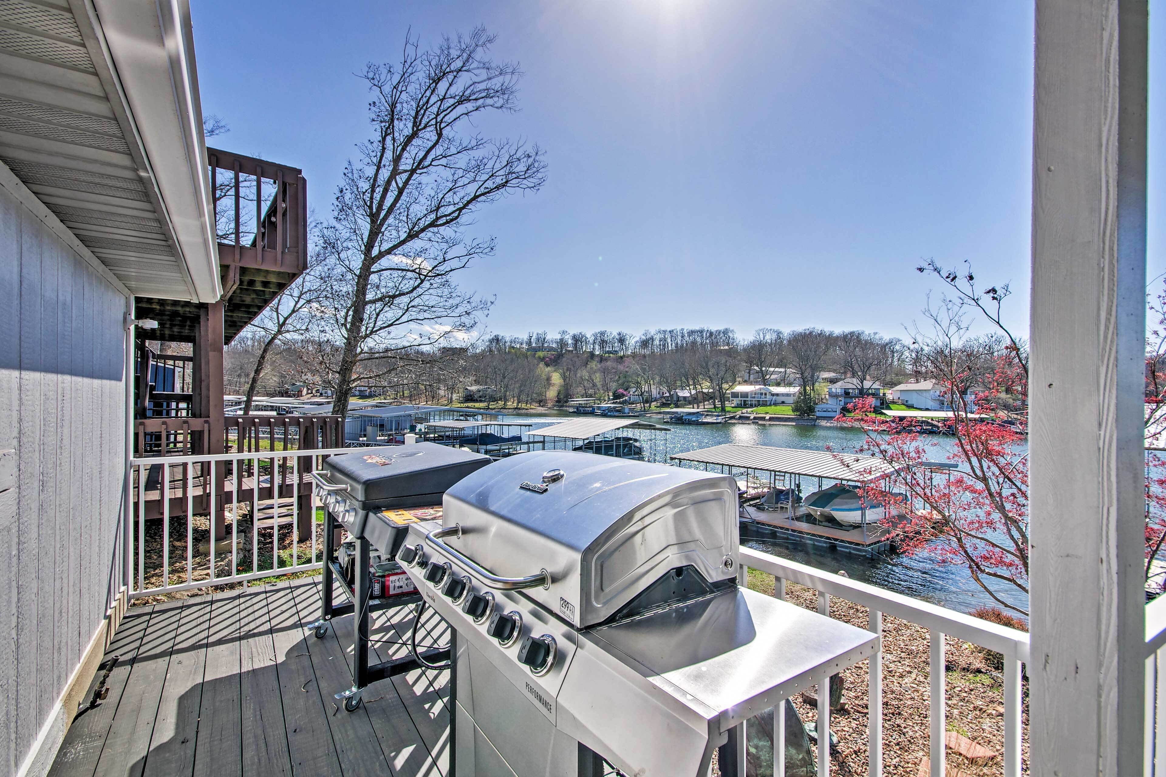 A deck with a barbecue grill and a view of a lake and boats.