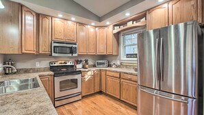 A kitchen with wooden cabinets, stainless steel appliances, granite countertops, and a window above the sink.