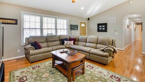 A living room with a sectional sofa, a wooden coffee table, a ceiling fan, and a large window.