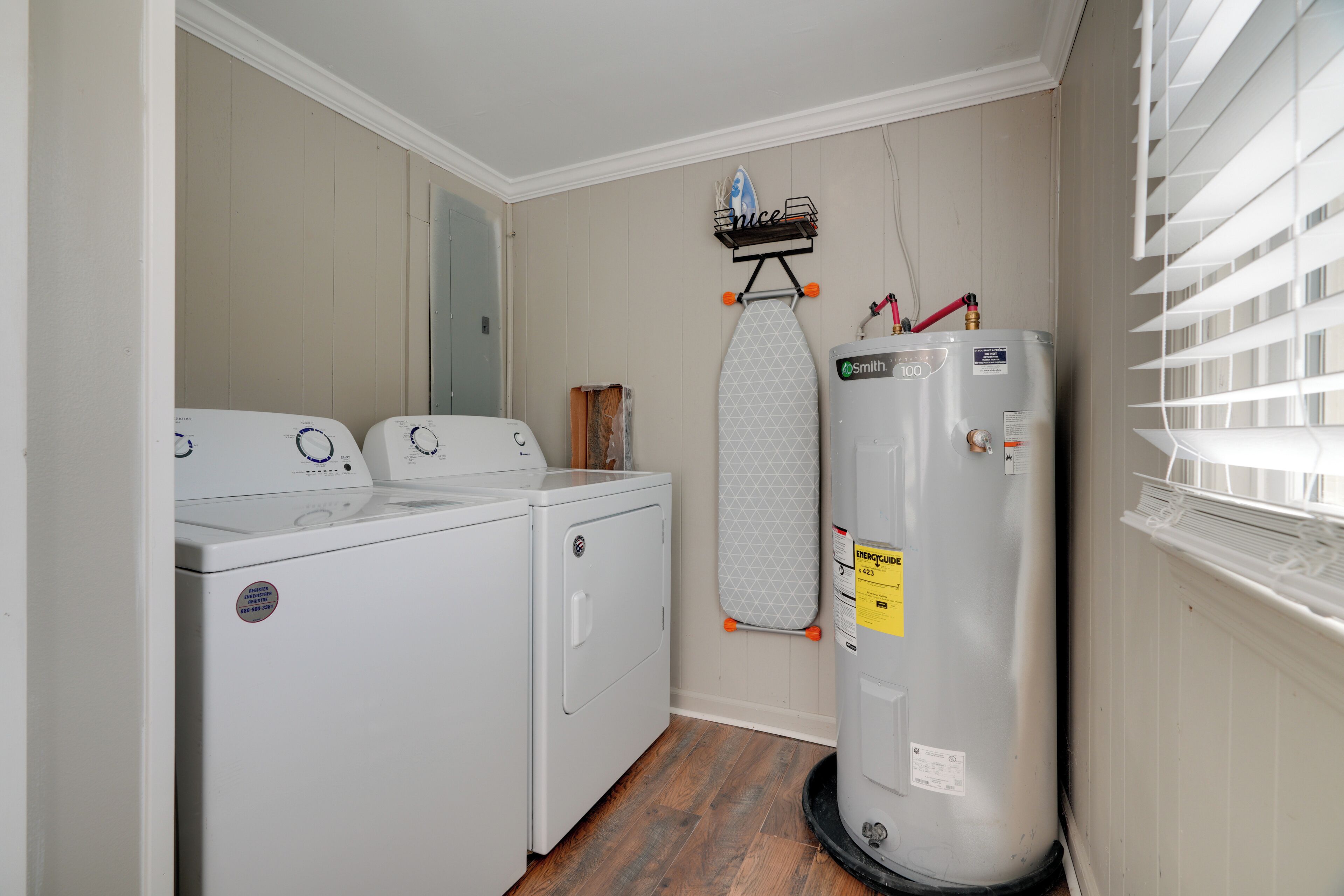 A laundry room with two front-loading washers, a stacked dryer, a water heater, and a wall-mounted ironing board.