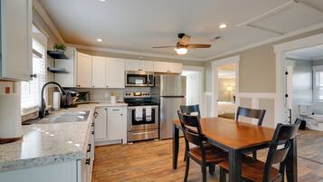 A modern kitchen with white cabinets, stainless steel appliances, a wooden dining table, and a ceiling fan.