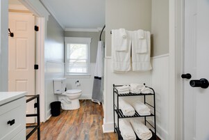 A bathroom with a wooden floor, white fixtures, a towel rack, and a shelf with folded towels.