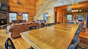 Une cabane en bois spacieuse, dotée d’une grande table à manger, d’un salon confortable avec une cheminée et d’une cuisine équipée d’appareils électroménagers modernes.