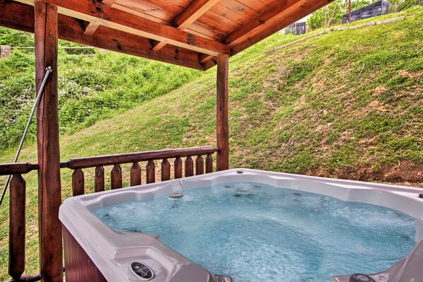 Un bain à remous sous une pergola en bois, avec une colline verdoyante en arrière-plan.