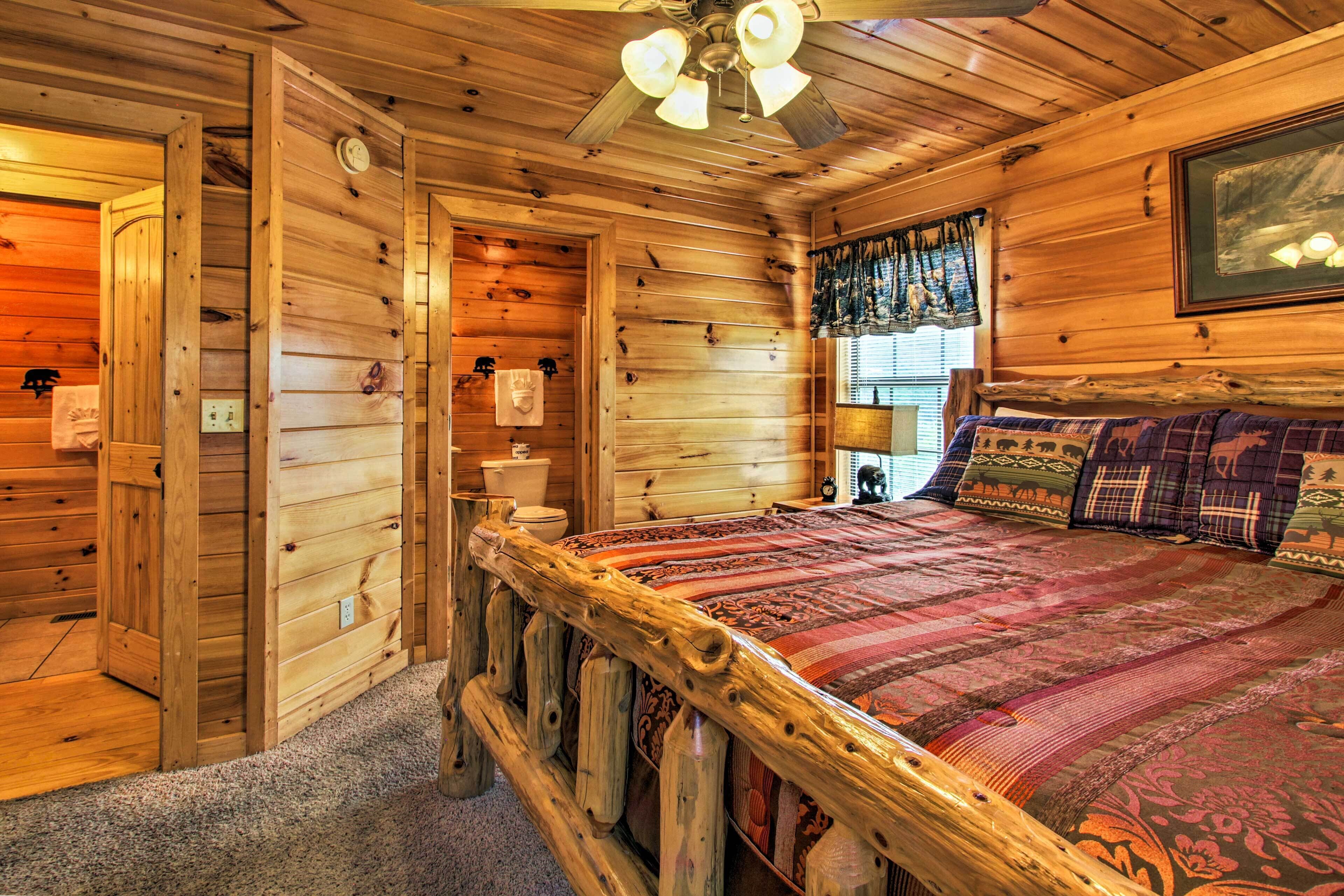 A wooden cabin interior with a bed, a ceiling fan, a window with curtains, and a framed picture on the wall.