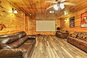 Une pièce chaleureuse avec un décor intérieur en bois, un ventilateur de plafond, un écran de projection et des canapés en cuir.