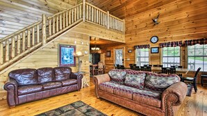 L’intérieur d’un chalet en bois comprend un escalier en bois, deux canapés en cuir, un coin repas et de grandes fenêtres.