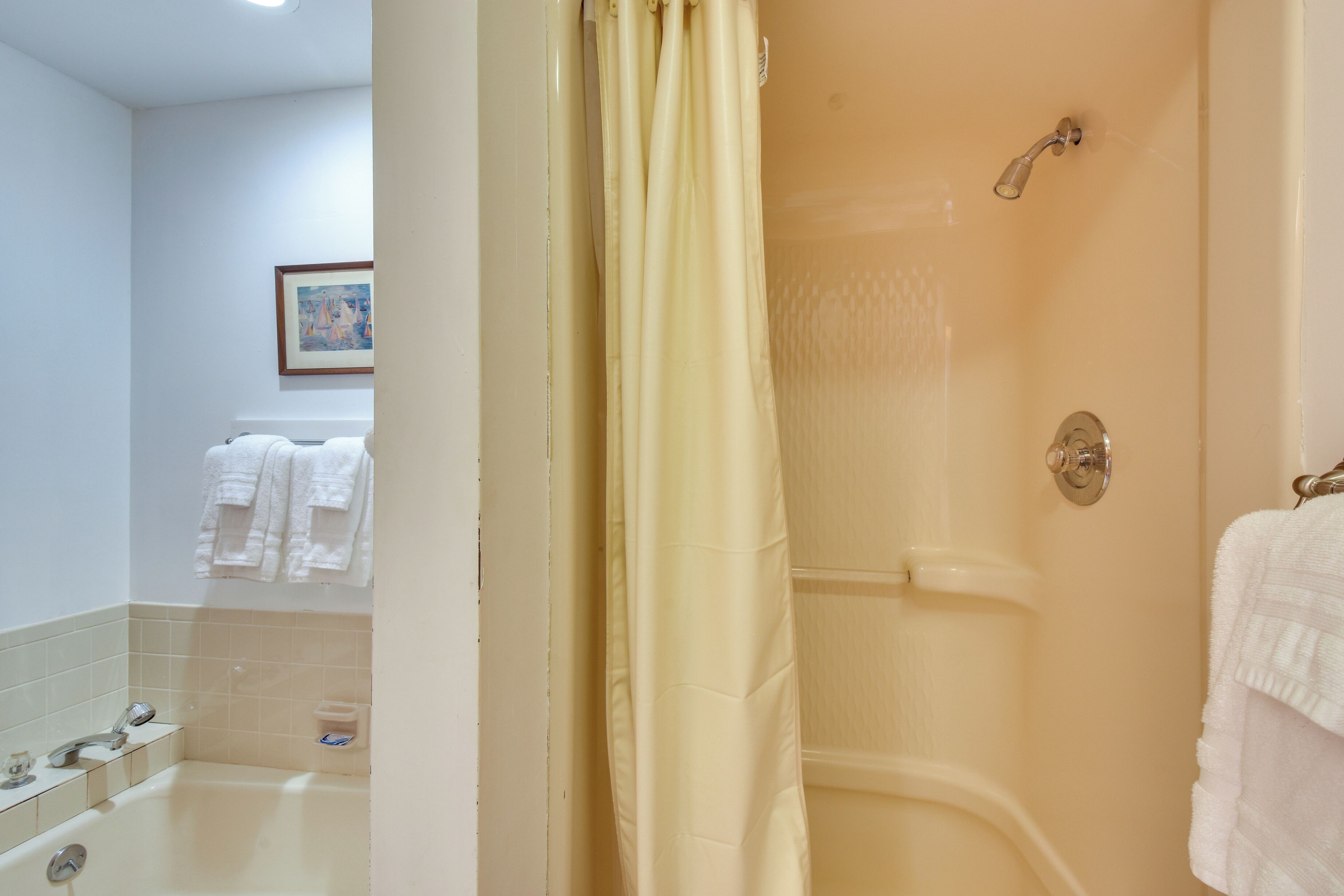 A bathroom with a bathtub, shower, and a toilet. There are towels hanging on the wall and a framed picture above the mirror.