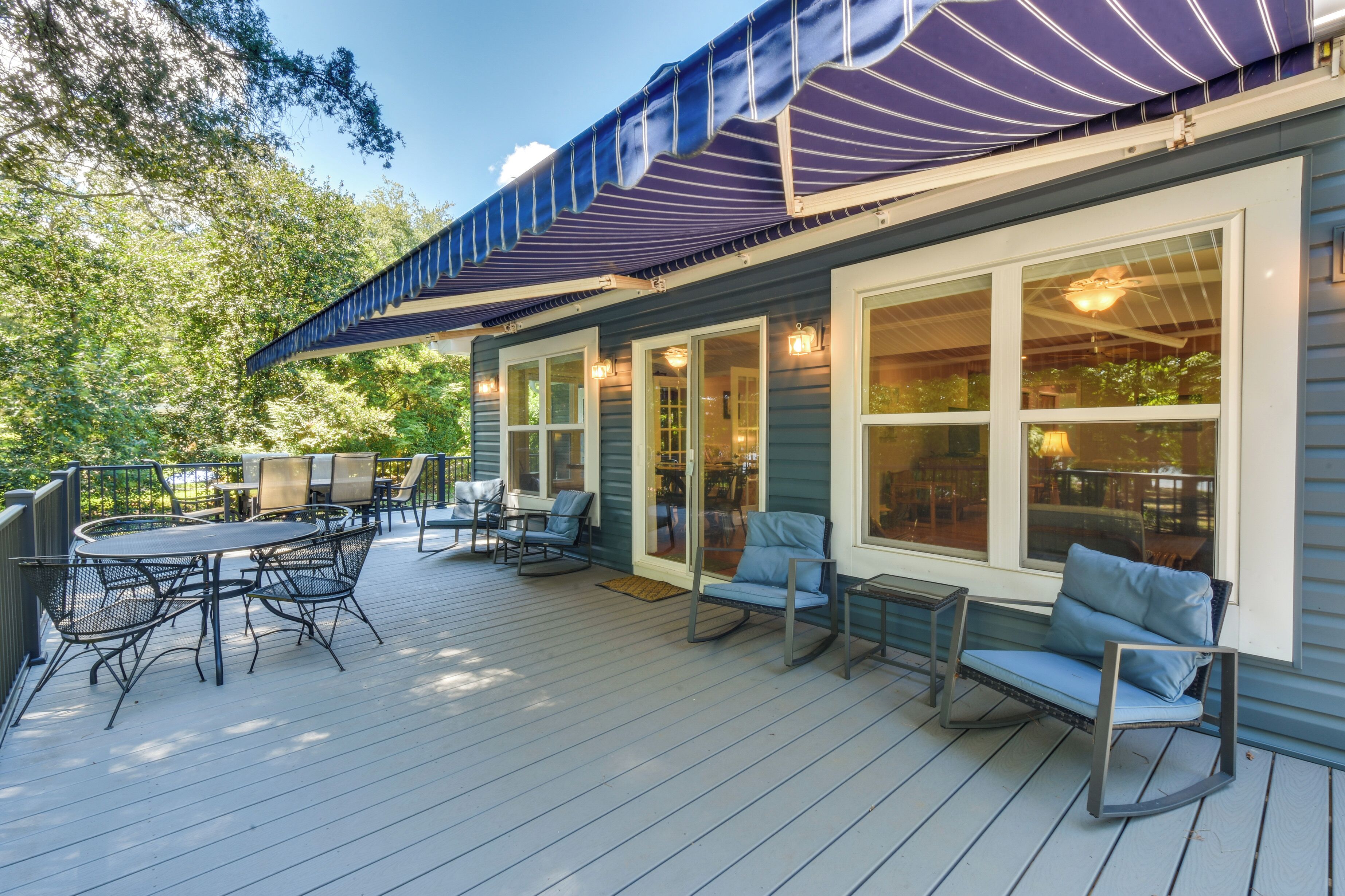 An outdoor deck with a dining table and chairs, a covered patio area, and a view of the surrounding trees.