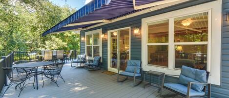 An outdoor deck with a dining table and chairs, a covered patio area, and a view of the surrounding trees.