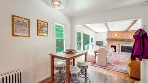 Un área de comedor con una mesa de madera y taburetes de bar, una lámpara colgante y cuadros en la pared.