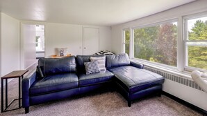 Una habitación con un sof á de cuero oscuro, una pequeña mesa de madera y vistas a árboles a través de un ventanal grande.