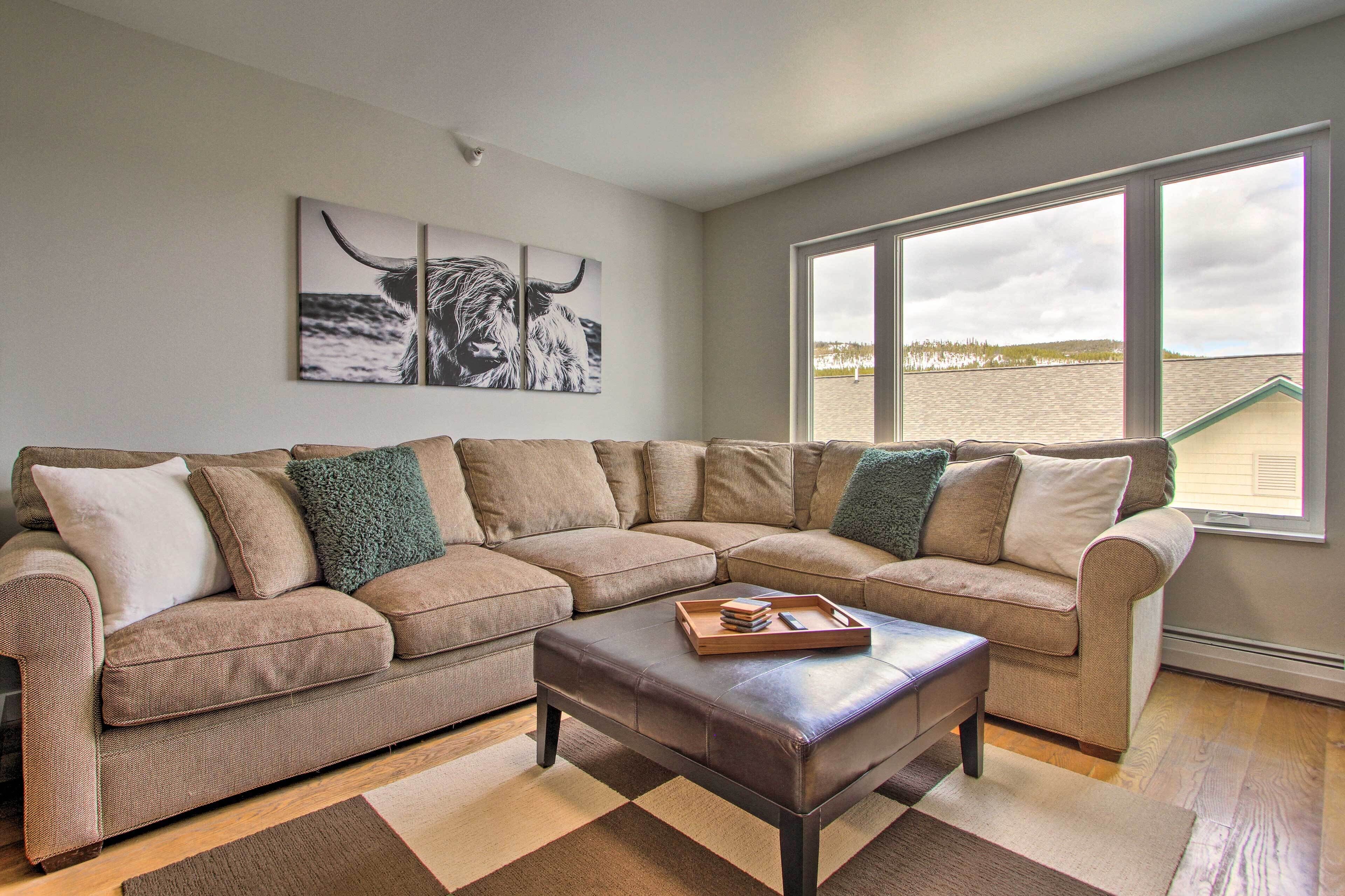 A living room with a sectional sofa, a coffee table, and a large window offering a view of the beach.