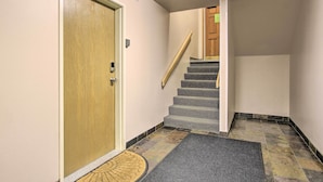 A hallway with a wooden door, a carpeted mat, and a staircase with a wooden handrail. - Cozy Montana Condo w/ Walk to Big Sky Resort! (Big Sky)