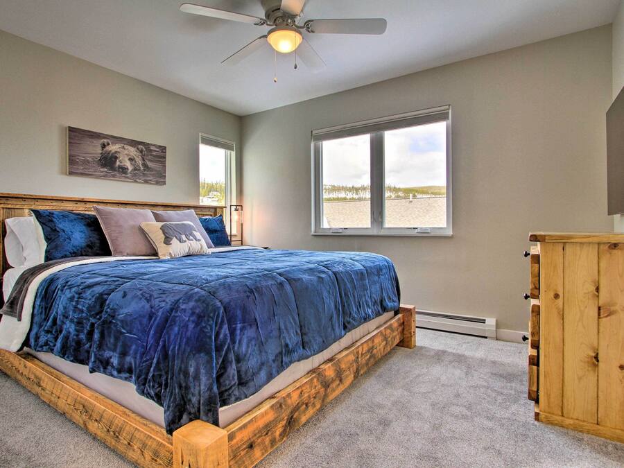 A bedroom with a large bed, a ceiling fan, a window with a view of the beach, and a wooden cabinet.