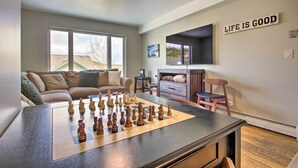 A living room with a chessboard, a sofa, a television, and a sign saying "LIFE IS GOOD". - Cozy Montana Condo w/ Walk to Big Sky Resort! (Big Sky)