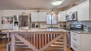 A kitchen with white cabinets, stainless steel appliances, a marble countertop, and a central island with a striped metal base. - Ruidoso Cabin - Walk to Midtown Dining & Shops! (Ruidoso)
