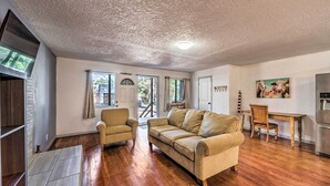 A spacious living area with a wooden floor, a beige sofa, a patterned armchair, and a dining table with chairs. - Ruidoso Cabin - Walk to Midtown Dining & Shops! (Ruidoso)