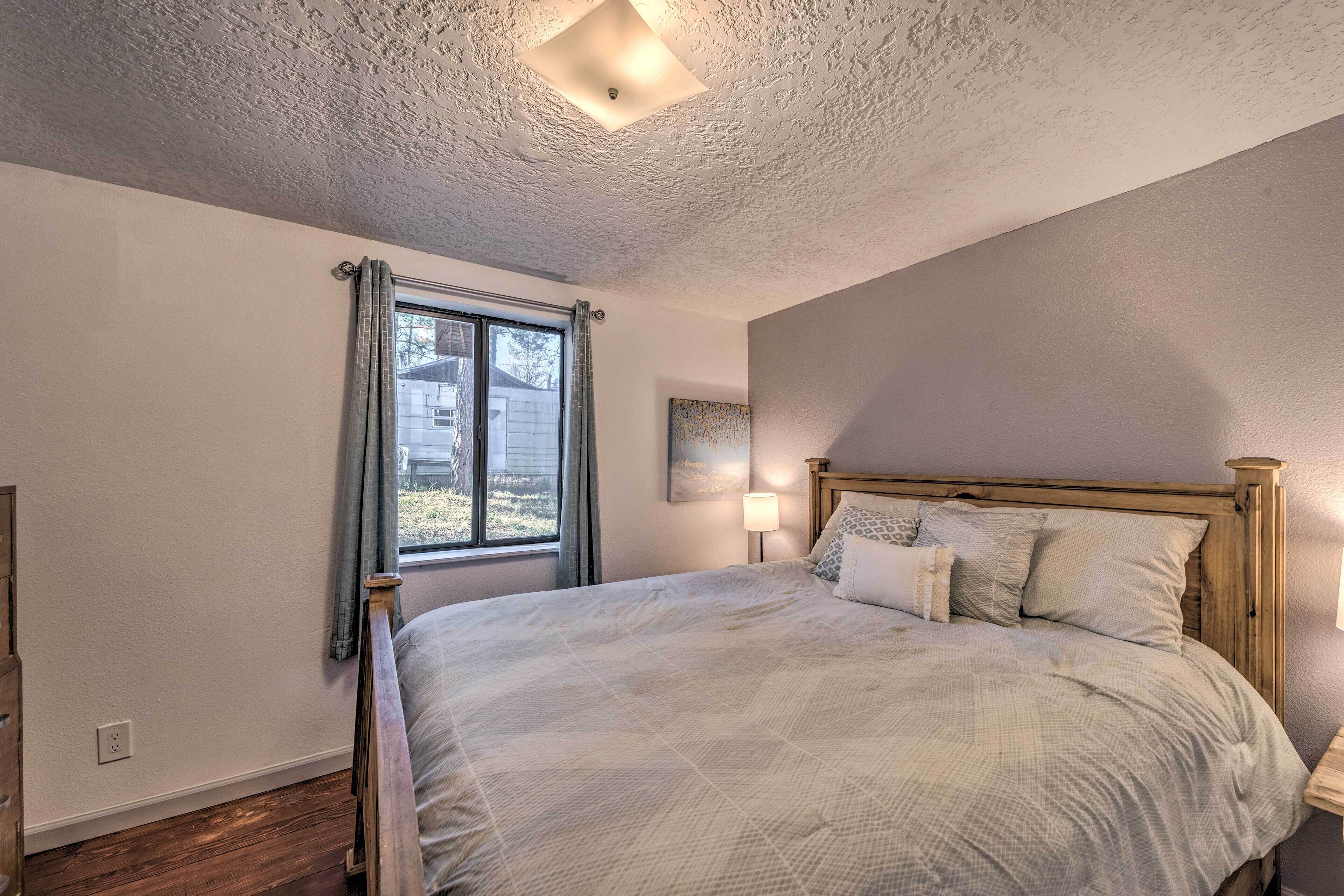 Ein Schlafzimmer mit einem Bett, einem Fenster mit Vorhängen, einem Nachttisch und einer Wandlampe.