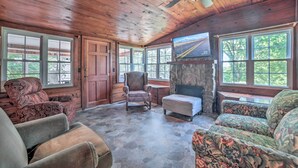 A cozy room with wooden ceilings, a stone fireplace, and large windows offering a view of the outdoors. - Rustic Dover Retreat w/ Porch - Walk to Boat Ramp! (Dover)