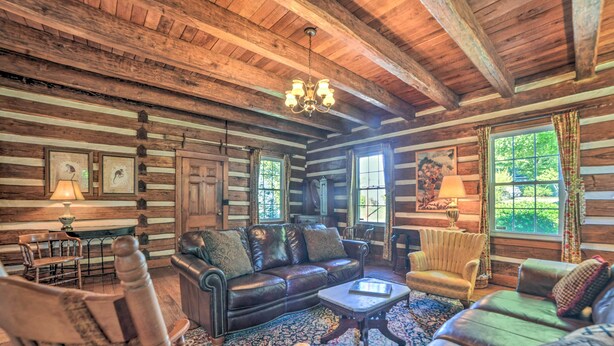 A log cabin interior with a leather sofa, armchairs, a chandelier, and a large window with curtains. - Rustic Dover Retreat w/ Porch - Walk to Boat Ramp! (Dover)