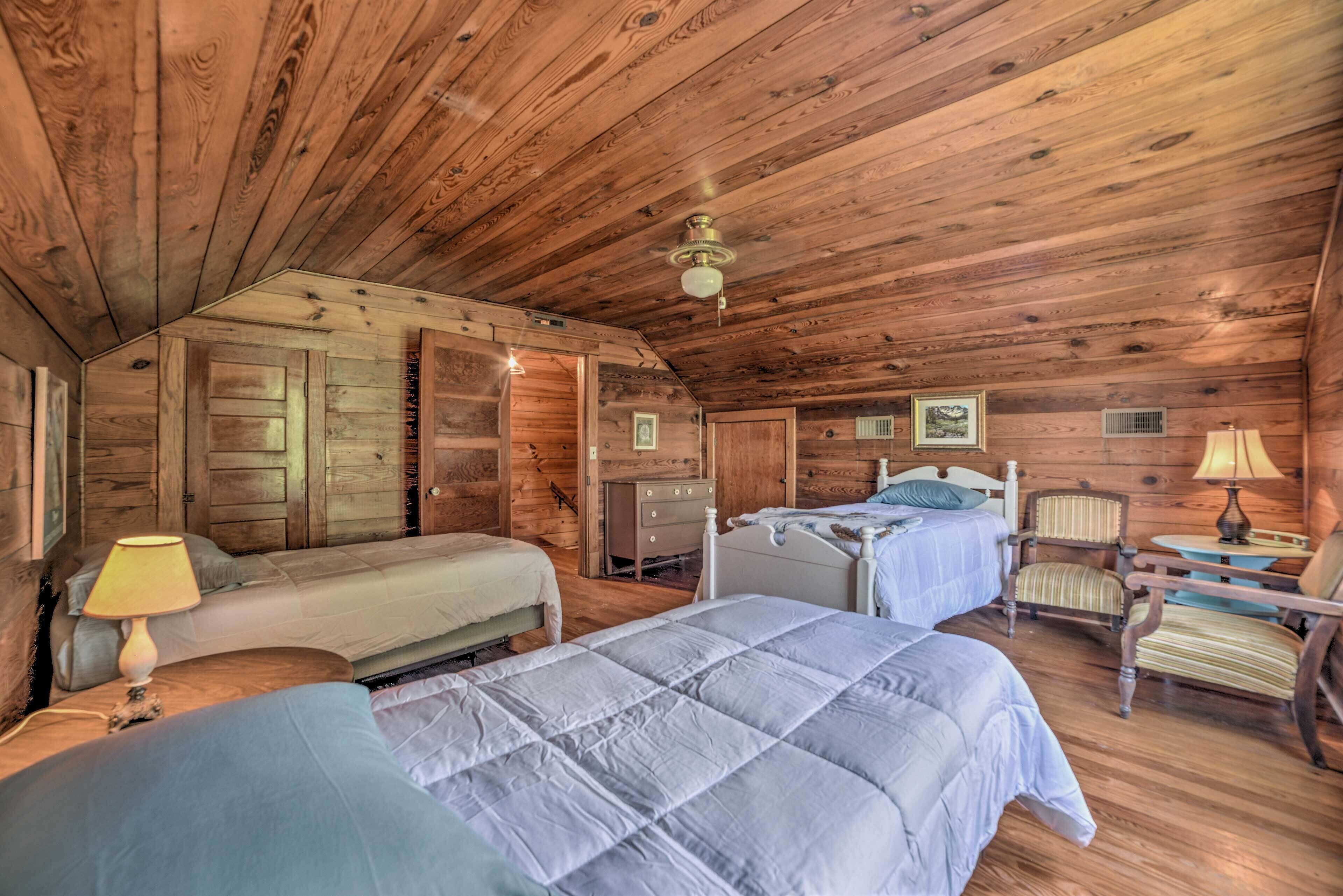 Un dormitorio tipo cabaña con dos camas, paredes de madera, un ventilador de techo y una mesita de noche con lámpara.