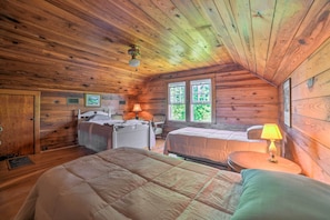 A cabin-style bedroom with wooden walls and a sloped ceiling. It includes two beds, a desk, and a chair.