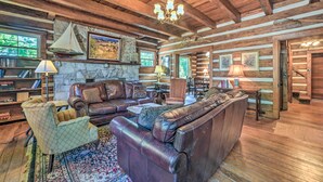 A log cabin interior with a leather sofa, armchairs, a fireplace, and a stone wall. - Rustic Dover Retreat w/ Porch - Walk to Boat Ramp! (Dover)