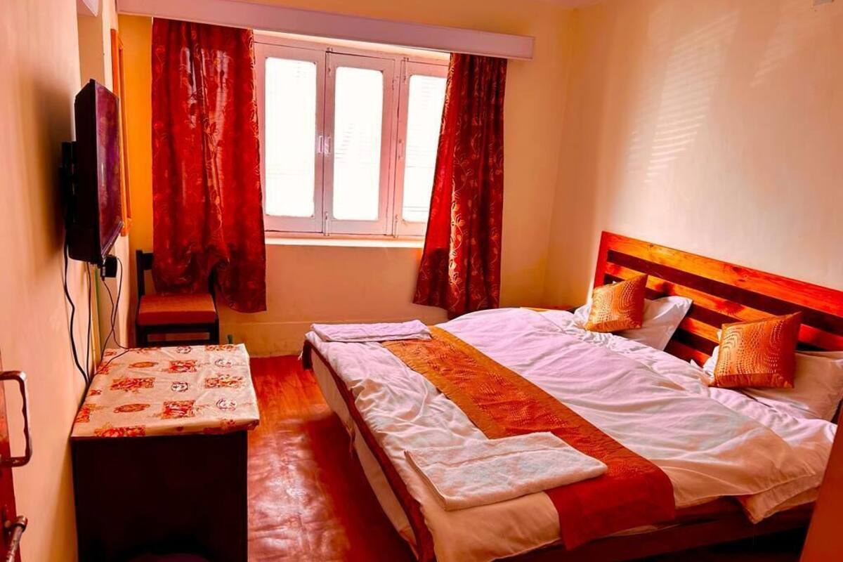 A hotel room with a bed, a TV, a small table, and a window with curtains.