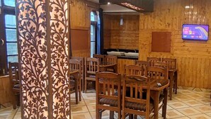 A wooden interior with multiple wooden tables and chairs, a television mounted on the wall, and a window with a view. - Hotel RI Rab (Leh)