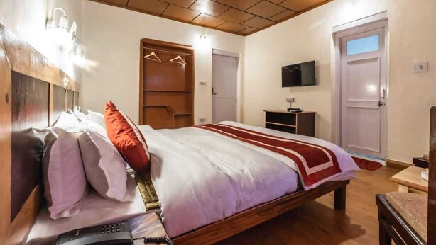 A hotel room with a wooden bed, bedside table, and a TV on the wall. - Hotel RI Rab (Leh)