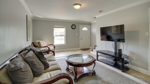 A living room with a sofa, a glass-top coffee table, a TV on a stand, a door, and a window. - Gulfport Condo w/ Private Balcony - Walk to Beach! (Gulfport)
