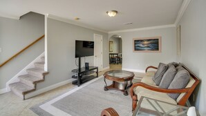 A living room with a staircase, a television, a dining area in the background, and a painting on the wall. - Gulfport Condo w/ Private Balcony - Walk to Beach! (Gulfport)
