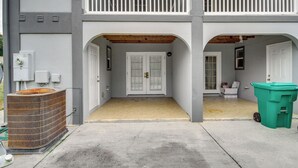 A two-story building with a covered front porch, a large air conditioning unit, and a green trash bin. - Gulfport Condo w/ Private Balcony - Walk to Beach! (Gulfport)